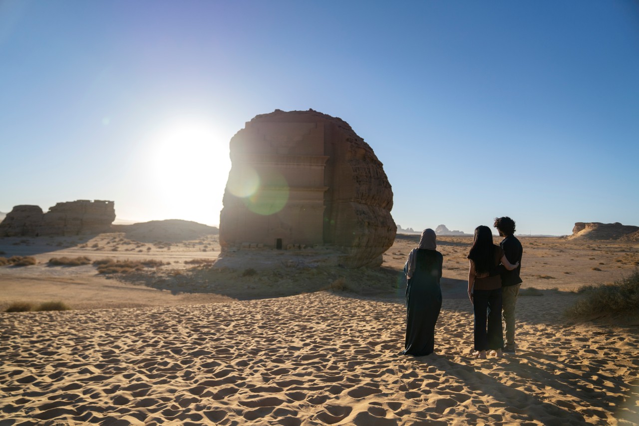 Visitors admiring the iconic Qasr al-Farid tomb at Hegra during golden hour