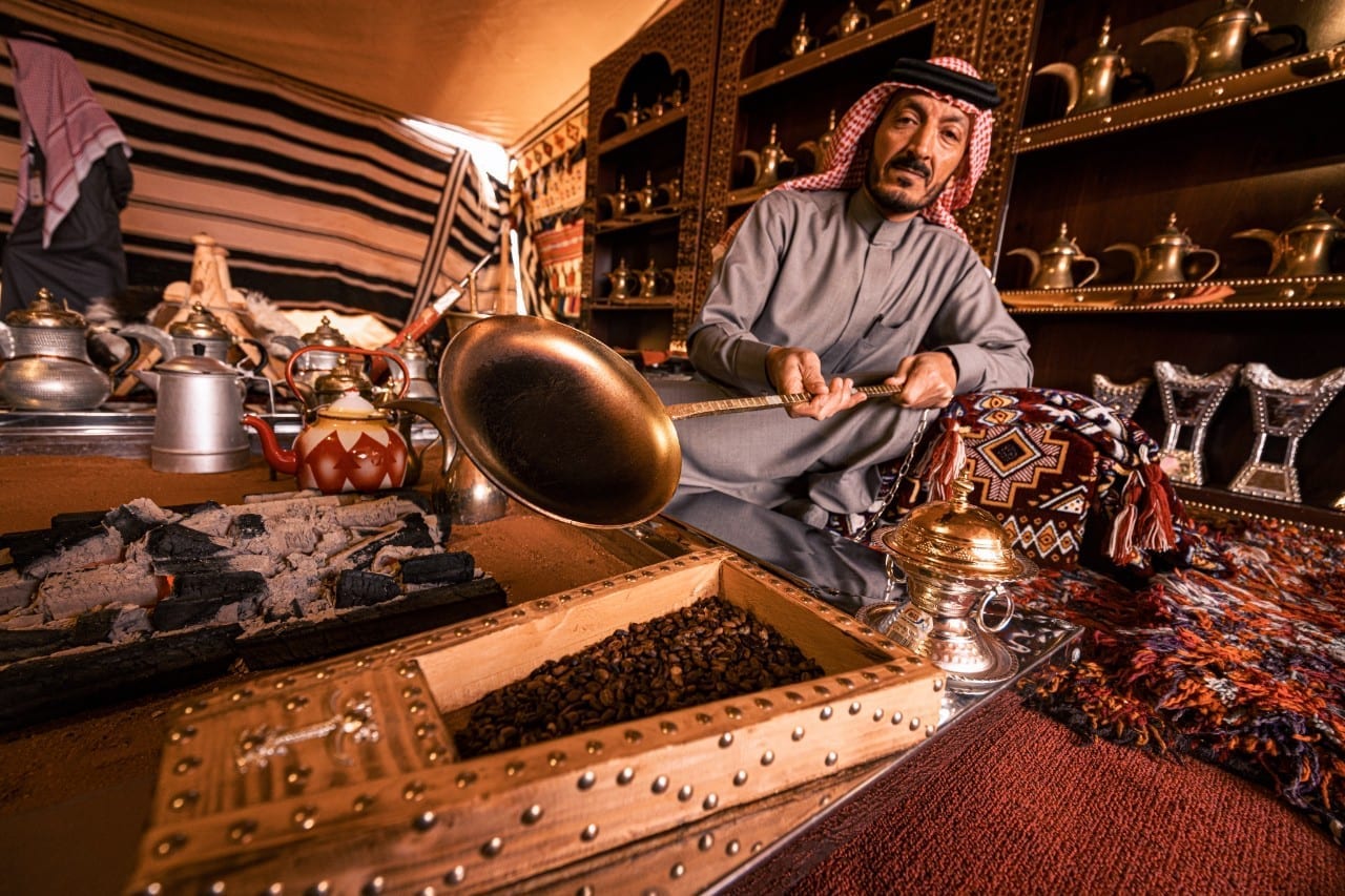 Traditional Bedouin man roasting coffee beans over an open fire in a tent