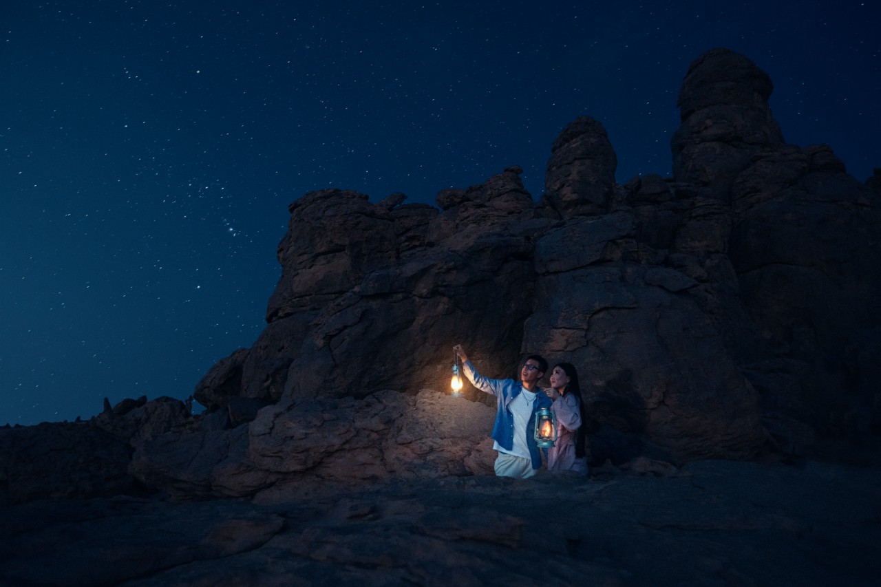 Couple with lantern beneath the stars at Elephant Rock (Jabal AlFil), AlUla, Saudi Arabia