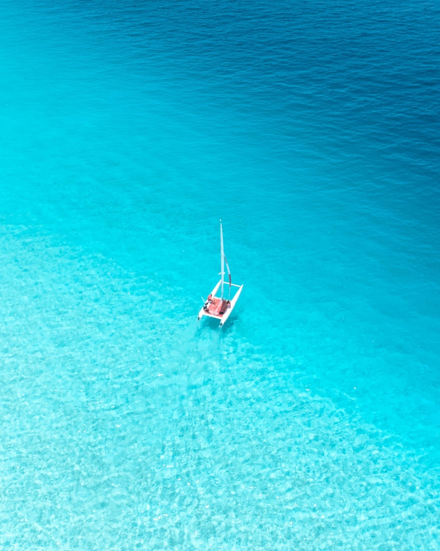 Aerial view of a sailboat on crystal-clear turquoise waters in the Saudi Red Sea