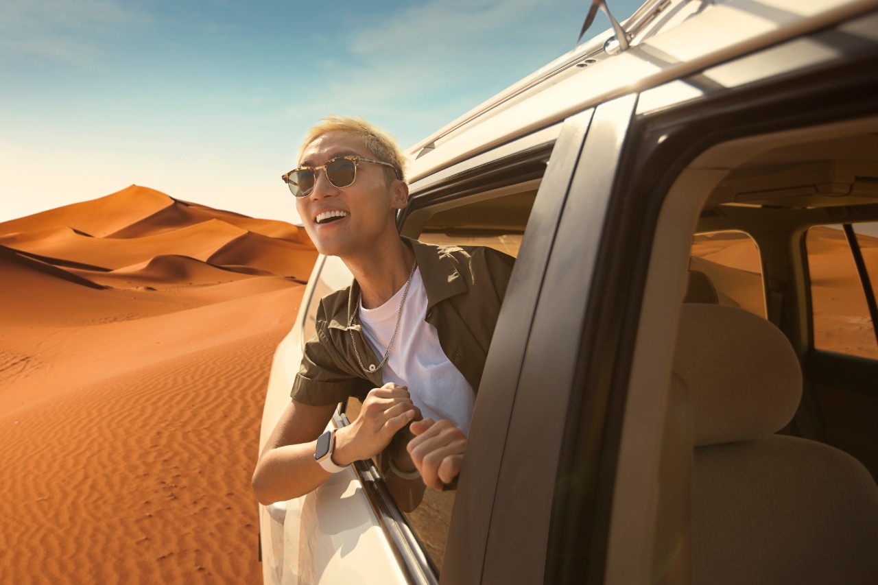 Luxury SUV transfer through Saudi Arabian desert dunes with traveler enjoying the landscape