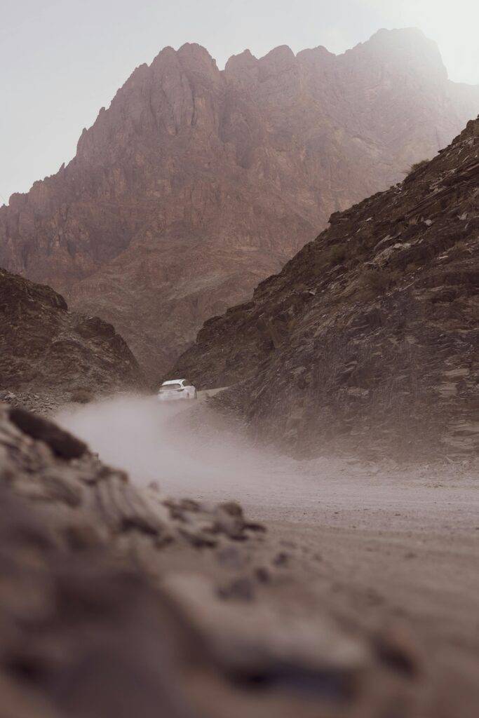 A white car travels on a dusty mountain road in Jabal Shams, Oman.