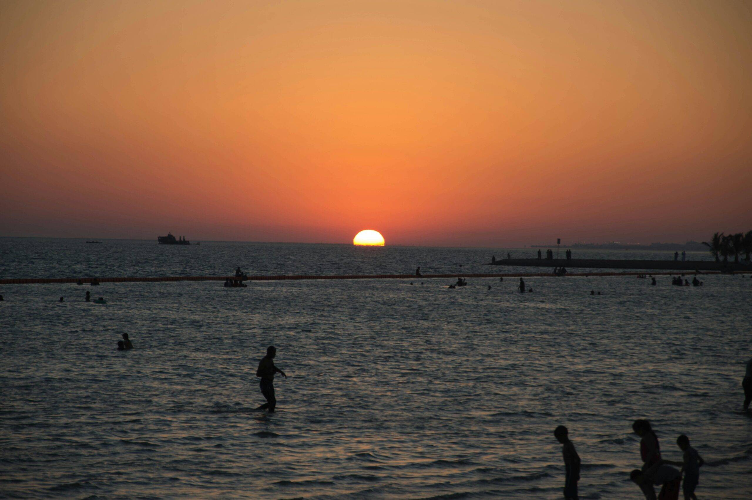 A stunning sunset at Yanbu beach with silhouettes of people enjoying the water.